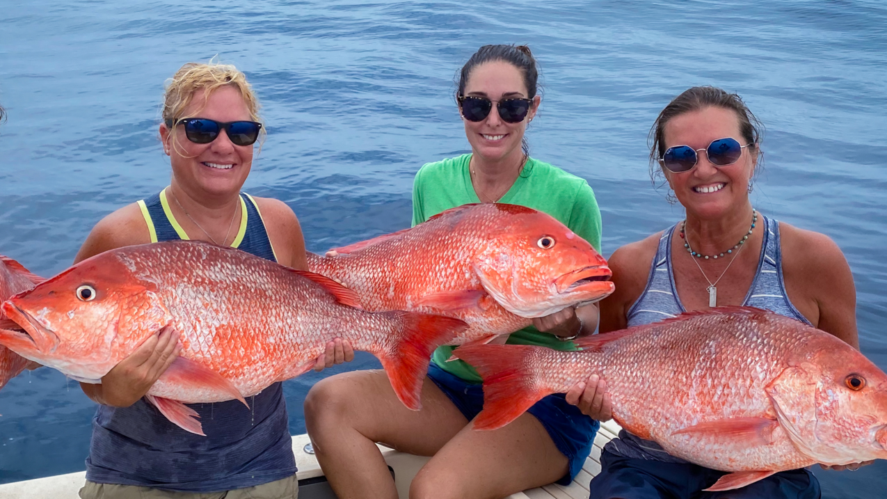 A group of women aboard a boat each hold a large red snapper.