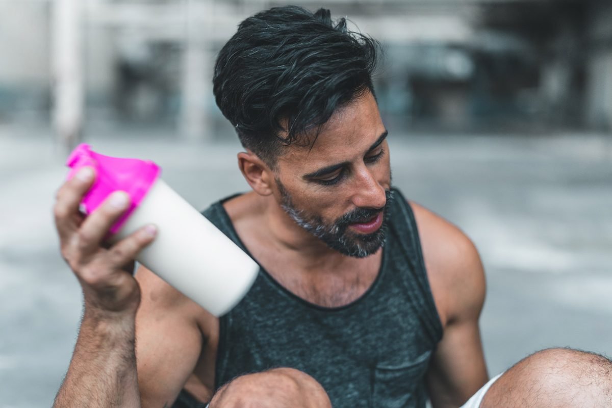A man is sitting down to mix a protein shake after en exercise inside an abandoned warehouse.
