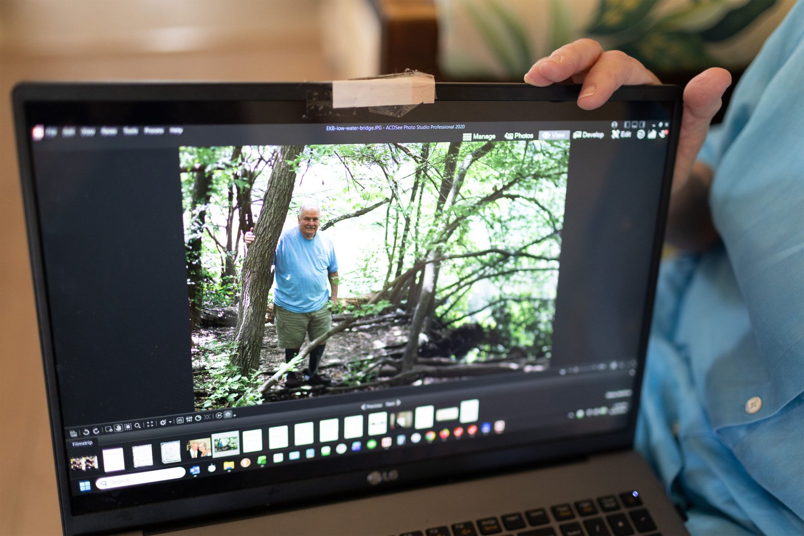 A photo of a man standing in the woods seen on a laptop.